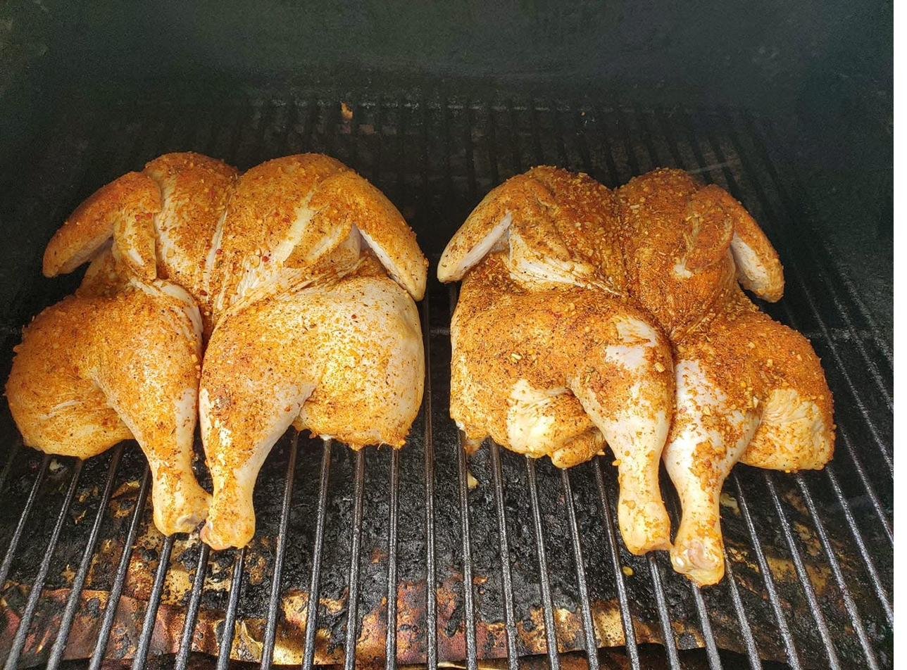 Two seasoned spatchcocked chickens on the smoker grate